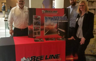 Bee Line Total Vehicle Wheel Alignment display with three professionals at a trade show, showcasing automotive alignment solutions.