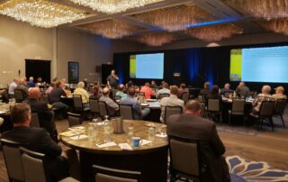 Audience attending a conference presentation with a speaker at the front, showcasing engagement in a professional setting.